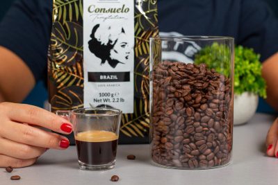 Granos de café Consuelo en un tarro transparente junto a un vaso de café
