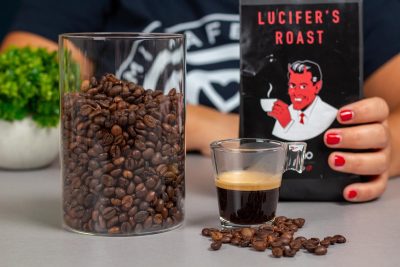 Vista en detalle de los granos de café Lucifer junto a una taza de café