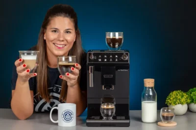 Verónica sujetando varios cafés junto a la cafetera Delonghi Autentica